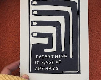 Op de afbeelding: Een zwart-wit kunstafdruk met de tekst "EVERYTHING IS MADE UP ANYWAYS". Het ontwerp toont een reeks verbonden, hoekige vormen. De afdruk is op getextureerd, gebroken wit papier.