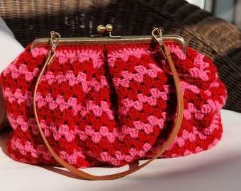Clutch de crochet rojo y rosa, con bandolera de color marrón claro.
