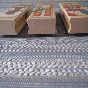 May include: Three wooden stamps featuring Christmas-themed illustrations. The stamps are rectangular with slightly rounded edges. The illustrations depict a snowman, Santa Claus, and a woman in a red dress.