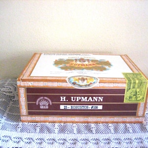 May include: A wooden box with a brown and gold label that reads "H. Upmann 1844 25 - Robustos - #100". The box is decorated with a gold and white design.
