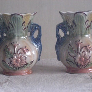 May include: Two vintage ceramic vases with blue handles and floral designs in shades of green, pink, and brown.