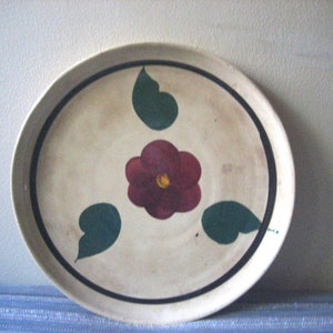 May include: A white ceramic plate with a black rim and a hand-painted design of a red flower with green leaves.