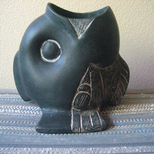 May include: A black ceramic fish-shaped planter with a carved design. The planter has a large, round eye and a textured surface.
