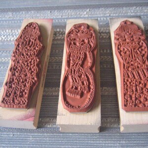 May include: Three wooden mounted rubber stamps with intricate designs. The stamps are all the same size and shape, but have different patterns. The patterns are all very detailed and intricate, and they are all in shades of red.
