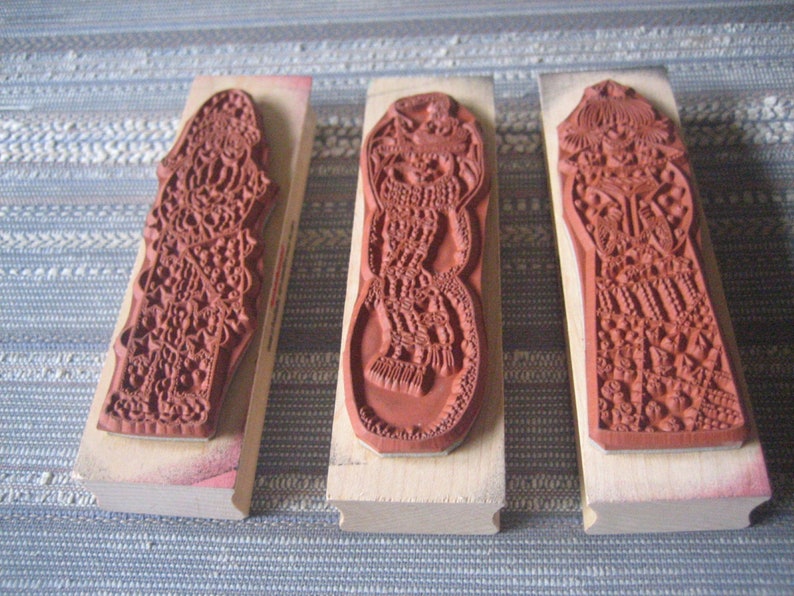 May include: Three wooden mounted rubber stamps with intricate designs. The stamps are all the same size and shape, but have different patterns. The patterns are all very detailed and intricate, and they are all in shades of red.