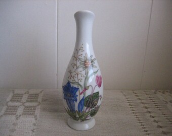 May include: A white ceramic vase with a floral design featuring blue, pink, and white flowers. The vase has a narrow neck and a rounded body.
