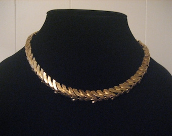 May include: A gold-toned chain necklace with a unique, geometric design. The chain is made up of interlocking links that form a series of pointed shapes.