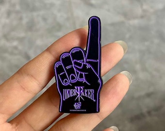 May include: Black and purple enamel pin in the shape of a hand with the index finger pointing up. The pin features the text "UNDERTAKER" in a stylized font, with the WWF logo at the bottom.