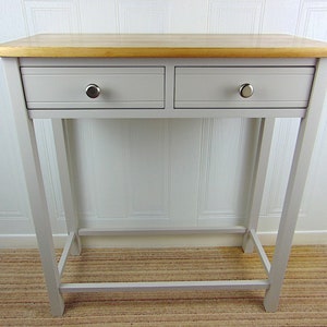 May include: A light grey console table with two drawers and a wood top. The table has a simple design with silver drawer pulls.
