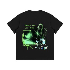 May include: A black short-sleeve t-shirt featuring a green graphic print on the back. The design includes the text "Meet me in the Wired." and "TRACKING," a stylized face, a starburst, a neuron-like structure, and scattered holographic CD shards.