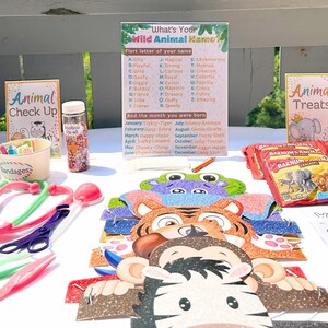 May include: A table set up for a children's party with a variety of animal-themed decorations and activities. There are animal masks, a sign that says "What's Your Wild Animal Kamo?" with a list of animals and their corresponding first letter of the alphabet, a sign that says "Animal Treats", and a bowl of sprinkles.