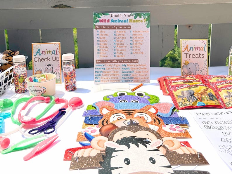 May include: A table set up for a children's party with a variety of animal-themed decorations and activities. There are animal masks, a sign that says "What's Your Wild Animal Kamo?" with a list of animals and their corresponding first letter of the alphabet, a sign that says "Animal Treats", and a bowl of sprinkles.