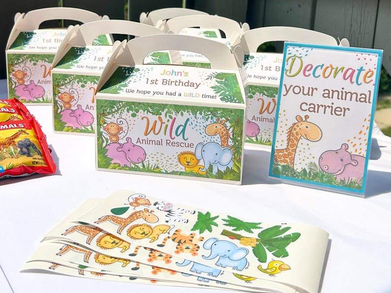 May include: A set of six colorful party favor boxes with a jungle animal theme. The boxes are decorated with a green, brown, and yellow jungle scene with a variety of animals, including a giraffe, elephant, monkey, and hippopotamus. The boxes are labeled "John's 1st Birthday" and "Wild Animal Rescue". A sign reads "Decorate your animal carrier".