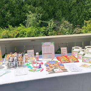 May include: A table set up for a wild animal themed party with decorations, games, and treats. There are stuffed animals, a sign that says "Adopt a Wild Animal", and a sign that says "Animal Treats".