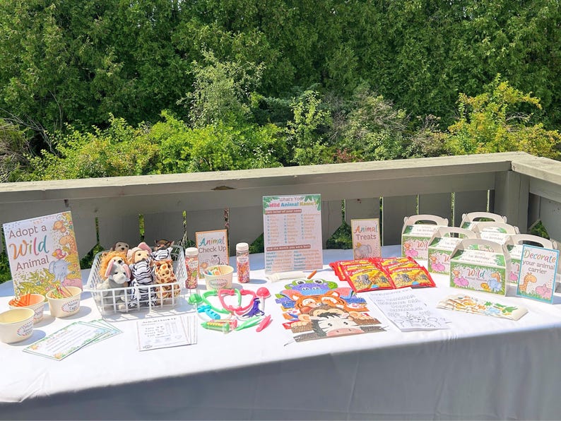 May include: A table set up for a wild animal themed party with decorations, games, and treats. There are stuffed animals, a sign that says "Adopt a Wild Animal", and a sign that says "Animal Treats".