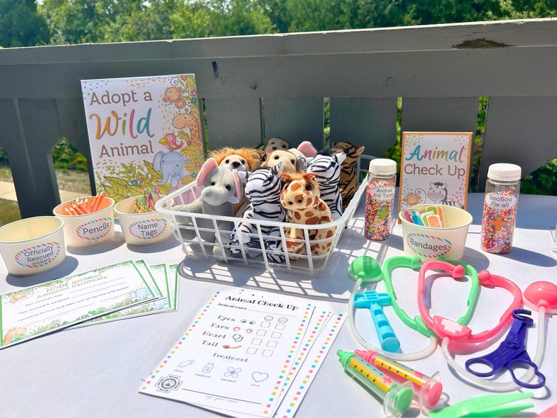 May include: A table set up for a children's animal adoption event. There are stuffed animals in a basket, pencils, name tags, and animal check-up forms. The sign says "Adopt a Wild Animal".