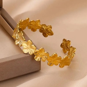 May include: A gold-toned bracelet featuring a floral design. The bracelet is made of metal and has a delicate, feminine look.