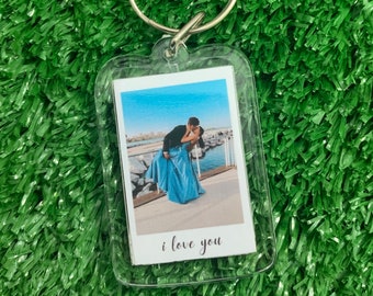 May include: Clear acrylic keychain with a photo of a couple kissing, with the words "i love you" printed below the photo. The keychain has a silver metal ring and is set against a green background.