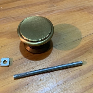 May include: A gold-toned round cabinet knob with a square metal washer and a long silver screw.