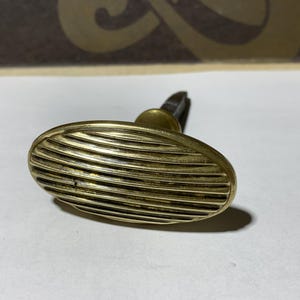 Puede incluir: Manija de puerta ovalada de latón antiguo con detalles de ranuras horizontales. El mango tiene una base pequeña y redonda y un accesorio rectangular. El latón tiene una apariencia ligeramente envejecida, lo que sugiere orígenes antiguos.