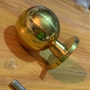 Peut inclure: Une poignée de porte dorée avec une poignée ronde et sphérique et une base plate et circulaire.