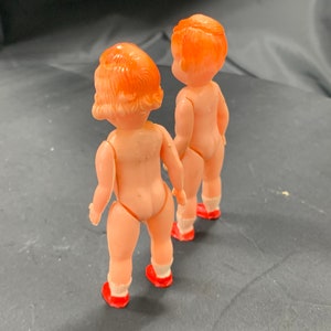 Pode incluir: Duas bonecas de pl&aacute;stico com sapatos vermelhos e cabelo laranja. As bonecas est&atilde;o de costas uma para a outra.