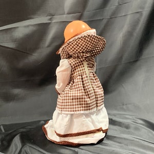 May include: A brown and white gingham dress with a white lace trim and a white collar. The dress has a zipper down the back and a brown hat with a white trim.
