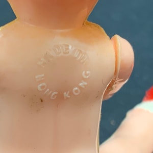Pode incluir: Um close-up de uma boneca de pl&aacute;stico rosa com um sapato vermelho. A boneca tem um c&iacute;rculo branco nas costas que diz "Made in Hong Kong".