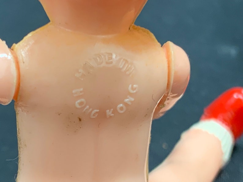 Pode incluir: Um close-up de uma boneca de pl&aacute;stico rosa com um sapato vermelho. A boneca tem um c&iacute;rculo branco nas costas que diz "Made in Hong Kong".