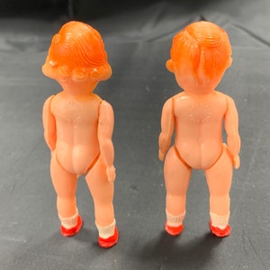 Pode incluir: Duas pequenas bonecas de pl&aacute;stico com cabelo ruivo e sapatos vermelhos. As bonecas est&atilde;o de costas uma para a outra.