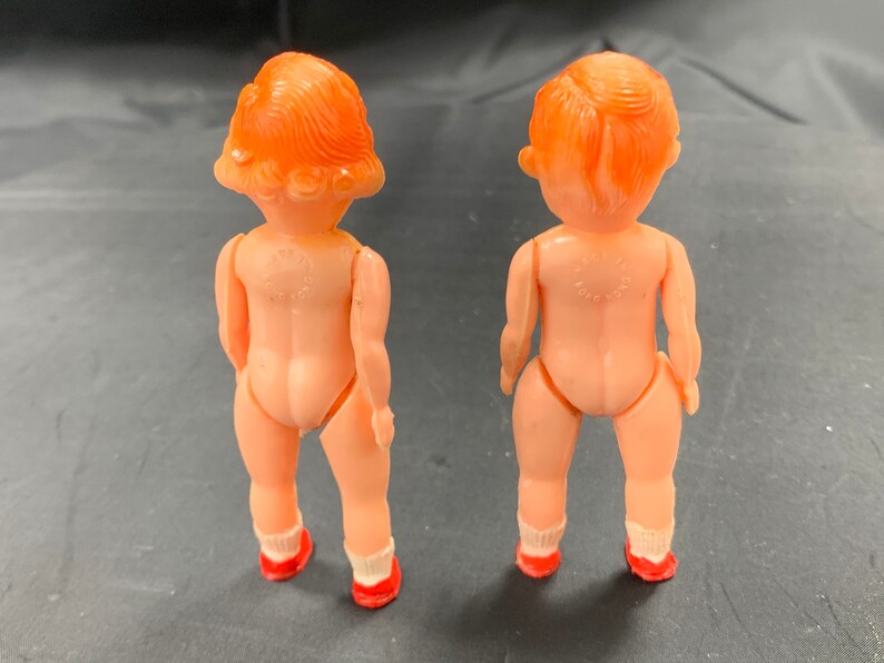 Pode incluir: Duas pequenas bonecas de pl&aacute;stico com cabelo ruivo e sapatos vermelhos. As bonecas est&atilde;o de costas uma para a outra.