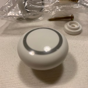 May include: White ceramic cabinet knob with a silver ring around the edge.