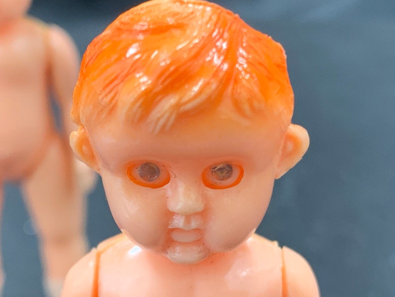 Pode incluir: Close-up do rosto de uma boneca de pl&aacute;stico com cabelo laranja e olhos castanhos. A boneca tem um sorriso pintado e bochechas rosadas.