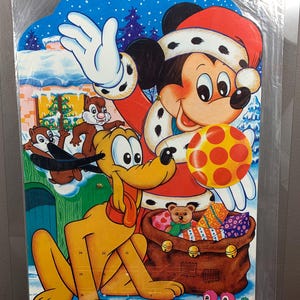 Pode incluir: Um calendário do advento de Natal vintage com o Mickey Mouse vestido de Papai Noel, segurando uma bola vermelha e branca com bolinhas. Pluto está sentado na frente do Mickey, e há dois esquilos e dois pássaros no fundo. O calendário tem 24 portas numeradas.