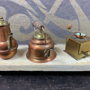 Peut inclure: Trois objets de cuisine miniatures antiques en cuivre et en laiton : une théière, une bouilloire et un moulin à café. Les objets sont disposés sur une surface en bois blanc.