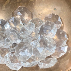 Peut inclure: Un tas de perles octogonales en verre transparent avec un trou au centre de chaque perle. Les perles sont dans un bol en laiton.