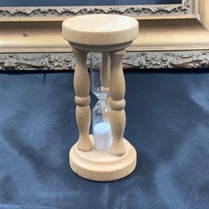 Puede incluir: Un reloj de arena de madera con un bulbo de vidrio transparente. El reloj de arena está sobre una superficie oscura.