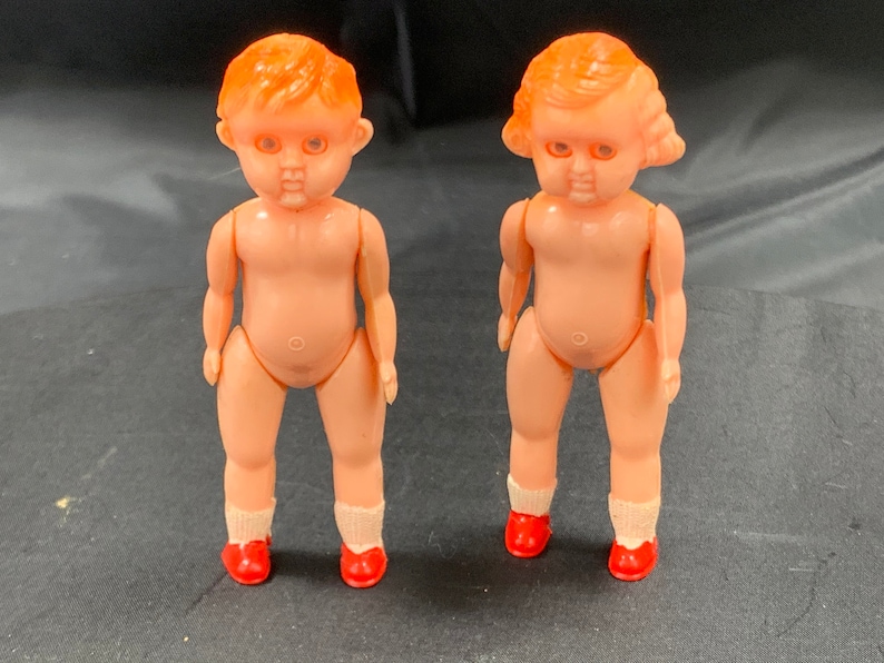Pode incluir: Duas bonecas de pl&aacute;stico com sapatos vermelhos e cabelo laranja. As bonecas est&atilde;o em p&eacute; sobre uma superf&iacute;cie preta.