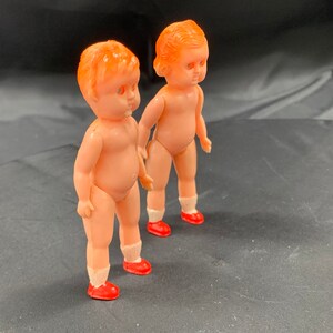 Pode incluir: Duas bonecas de pl&aacute;stico com cabelo laranja e sapatos vermelhos. As bonecas est&atilde;o em p&eacute; sobre uma superf&iacute;cie preta.