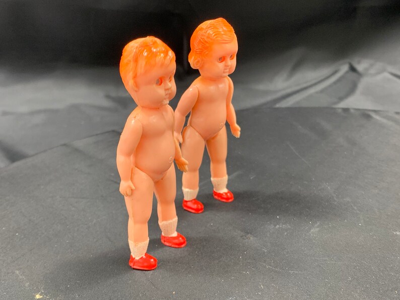 Pode incluir: Duas bonecas de pl&aacute;stico com cabelo laranja e sapatos vermelhos. As bonecas est&atilde;o em p&eacute; sobre uma superf&iacute;cie preta.