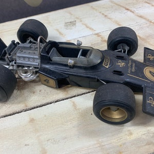 May include: Black and gold toy car model of a Lotus John Player Special Formula 1 race car. The car has a detailed engine and the number 4 on the side.