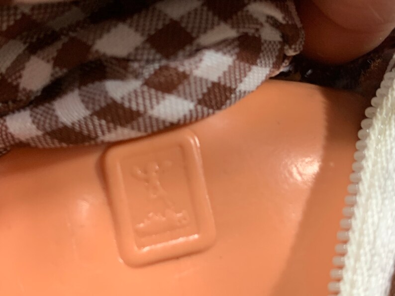 May include: Close-up of a brown and white checkered fabric with a brown plastic tag that has a stylized image of a person standing on a platform. The tag is attached to a brown fabric item.