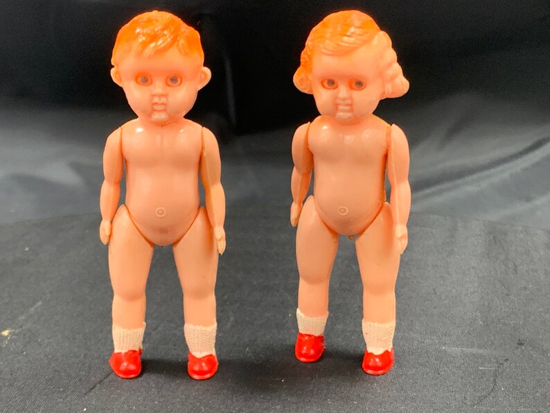 Pode incluir: Duas pequenas bonecas de pl&aacute;stico com cabelo ruivo e sapatos vermelhos. As bonecas s&atilde;o nuas e t&ecirc;m tra&ccedil;os faciais pintados.