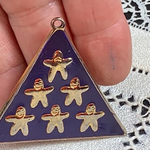 May include: A triangular pendant with a dark blue enamel background and a gold-colored border. The pendant features six gold-colored star-shaped figures. The pendant has a small loop at the top for hanging.