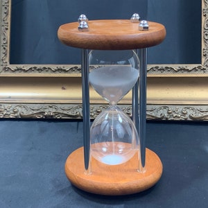 May include: A wooden hourglass with a silver frame and white sand. The hourglass is on a wooden base with silver accents.