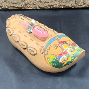 May include: A wooden clog with a painted scene of a windmill and the word "Holland". The clog has a small hourglass with pink sand inside.