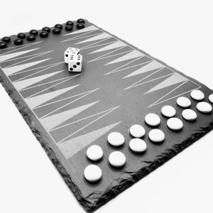 Könnte beinhalten: Ein schwarzes Schiefer-Backgammon-Brett mit weißen und schwarzen Spielsteinen. Zwei weiße Würfel liegen auf dem Brett.