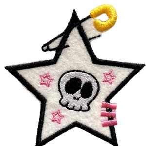 May include: White felt star with a black outline and a pink skull in the center. The star has four pink stars around the skull and a yellow loop at the top.