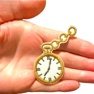 May include: Gold embroidered iron-on patch of a pocket watch with a chain. The watch face has black Roman numeral hour markers and black hands.