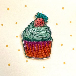 Puede incluir: Cupcake bordado en verde y naranja con una fresa roja y blanca en la parte superior.